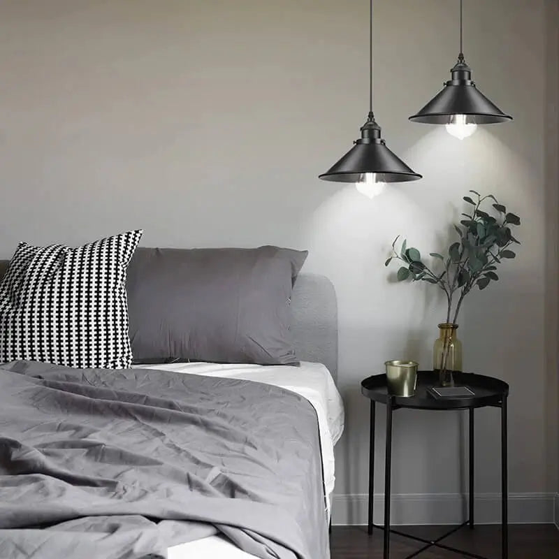 Two black pendant lights installed as bedside lighting above a nightstand in a modern bedroom with grey bedding.