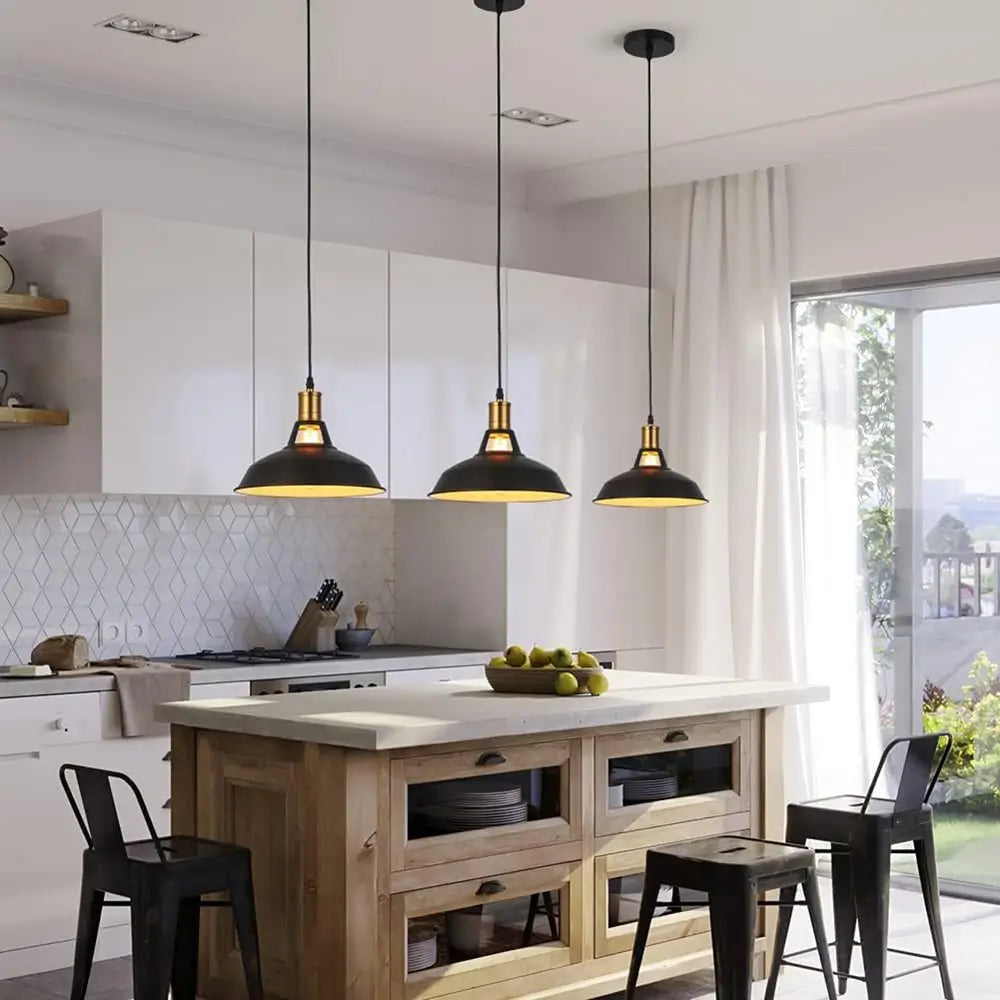 Three matte black industrial pendant lights with white interiors and brass sockets illuminating a rustic wooden kitchen island.