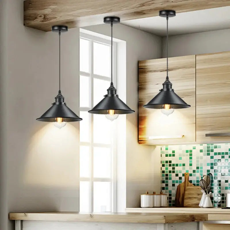 Three black farmhouse pendant lights hanging in a rustic kitchen above a wooden countertop with a window and tiled backsplash.