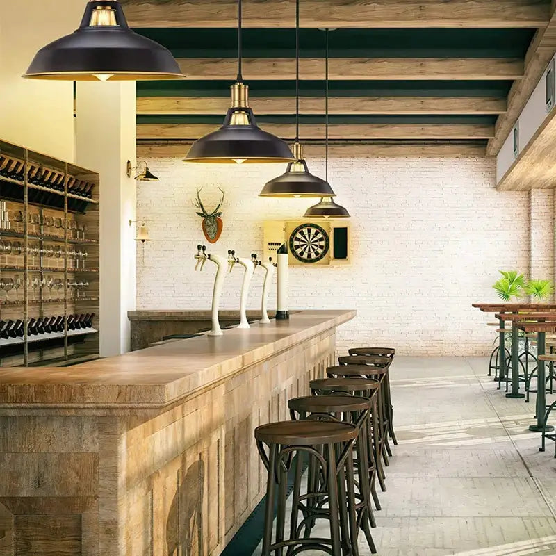 Multiple all-black industrial farmhouse pendant lights with brass sockets hanging above a long wooden bar counter in a rustic commercial bar or restaurant.