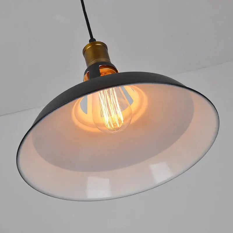 Close-up view of the matte black dome shade interior and vintage-style Edison bulb inside the industrial pendant light, highlighting the warm glow.