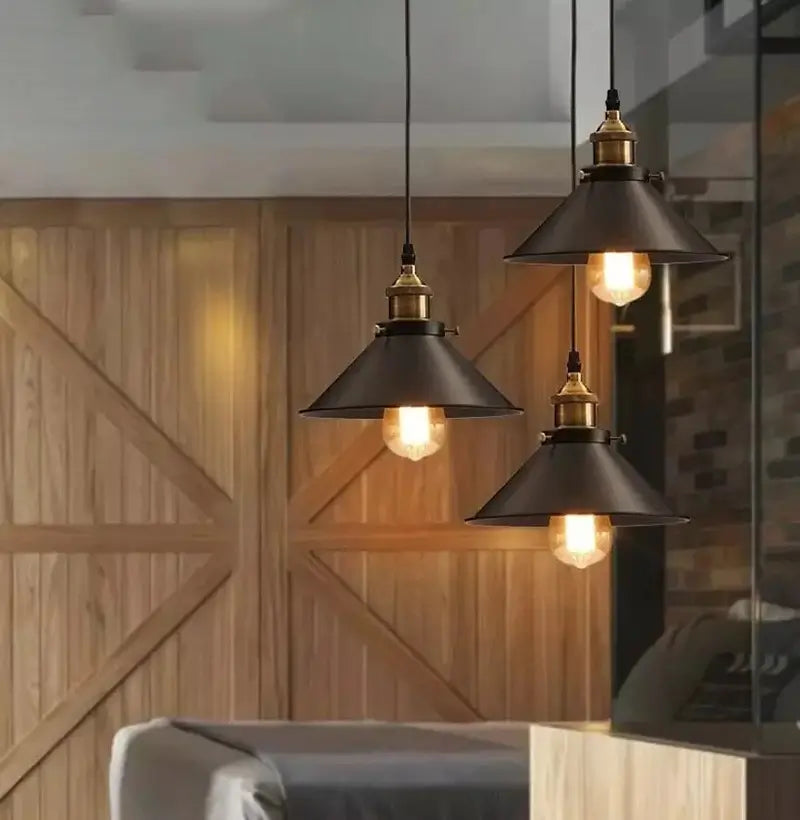 Close-up view of three black and brass pendant lights with warm Edison bulbs, illuminating a wooden wall and living space.