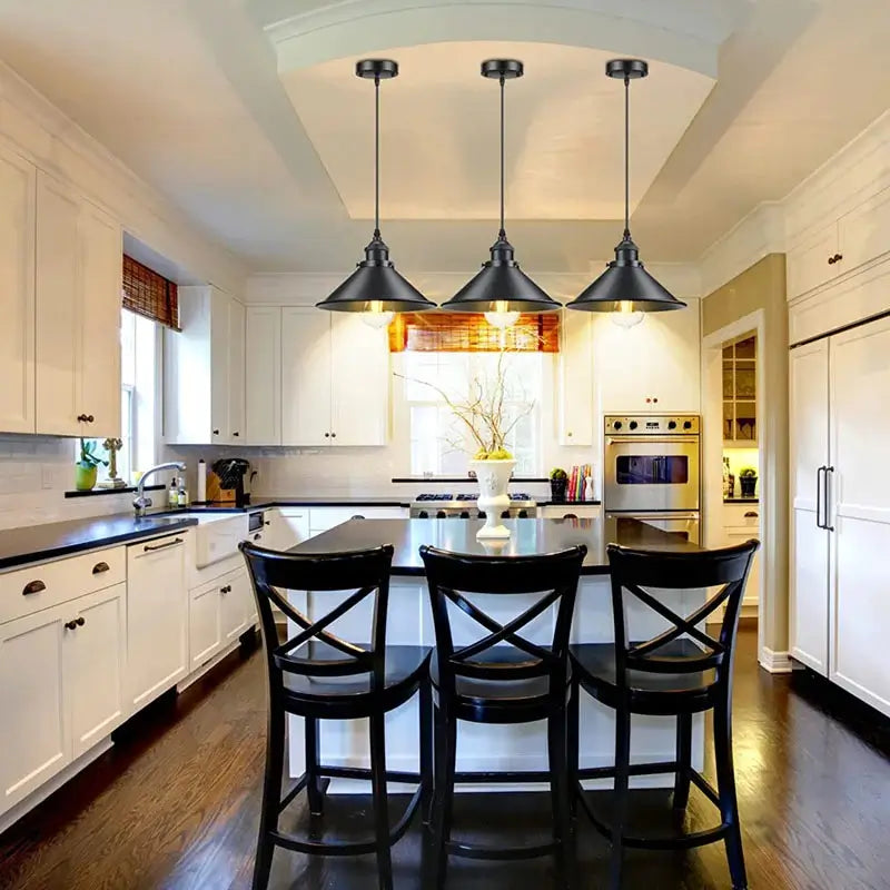 Three black industrial pendant lights illuminating a white kitchen island with black bar stools and white cabinets.