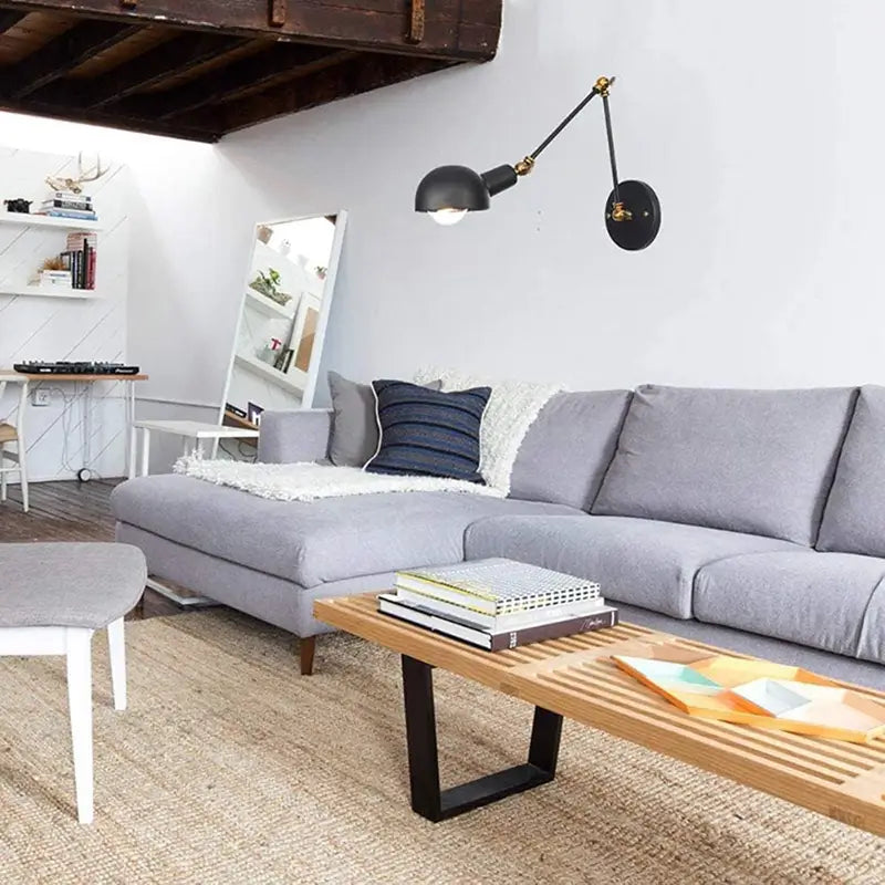 Adjustable black swing arm wall light installed in a modern loft-style living room, providing warm ambient lighting above a gray sofa.