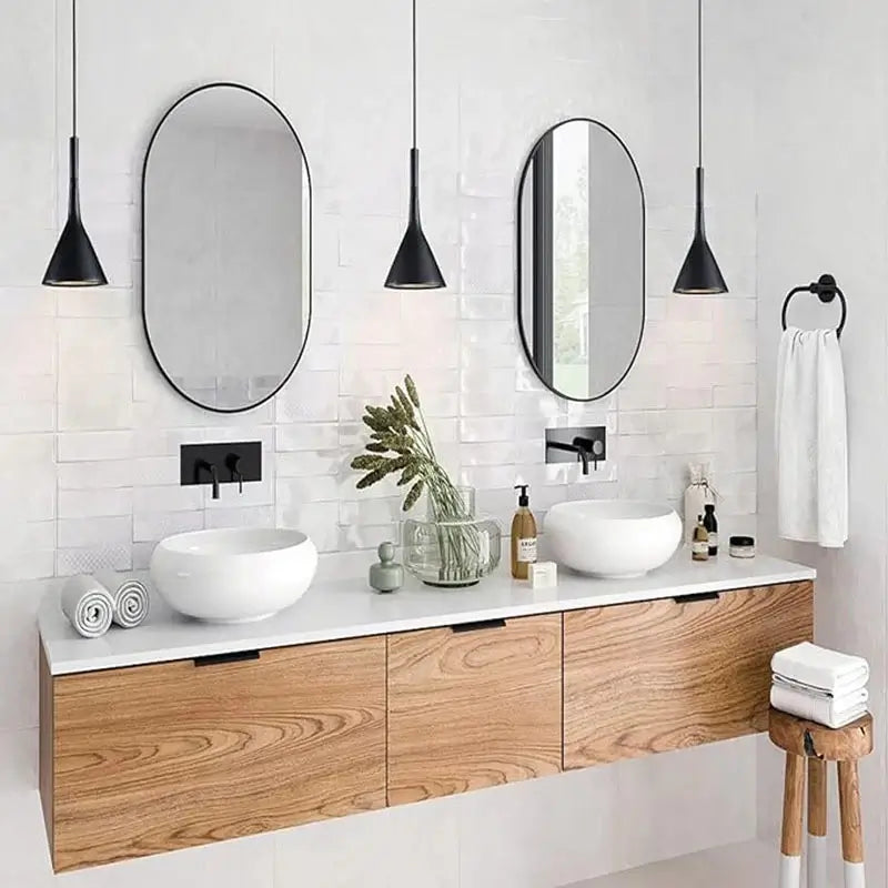 Two elegant black pendant lights above a double bathroom vanity with oval mirrors and white sinks, offering contemporary bathroom lighting for homes.