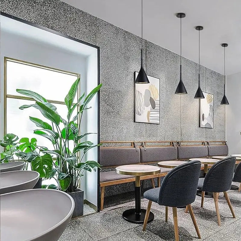 Multiple black cone pendant lights suspended in a modern cafe interior with grey textured walls and minimalist seating, providing stylish commercial lighting solutions.
