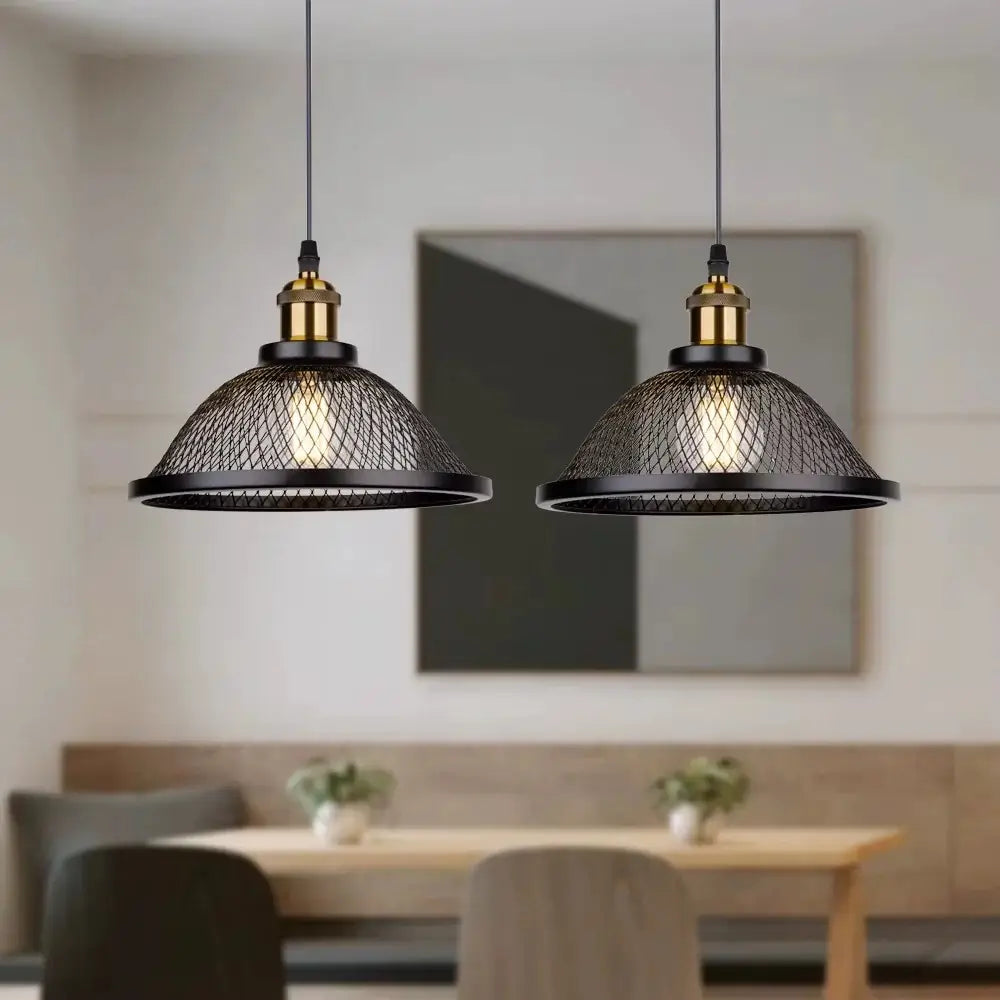 Two black industrial style hanging pendant lights with mesh shades and brass hardware, illuminating a cozy kitchen or dining area with a wooden table and bench seating.