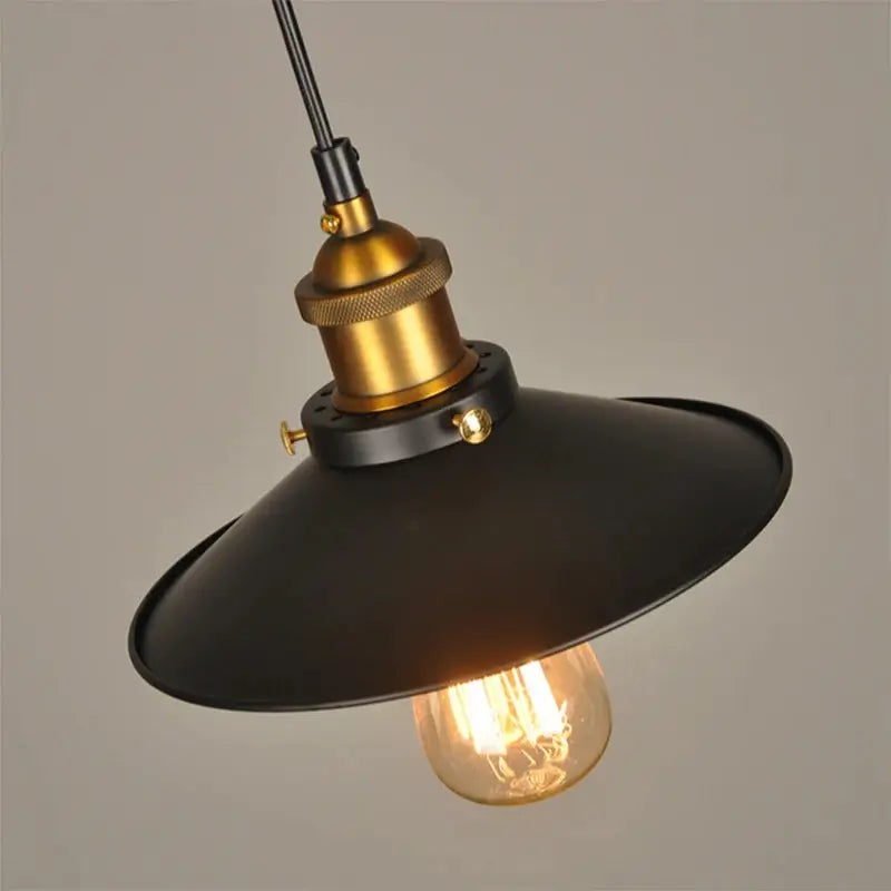Close-up of a black metal dome pendant light with brass accents and a warm Edison bulb, ideal for kitchen lighting.