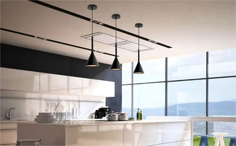 hree black minimalist pendant lights suspended over a clean, modern kitchen island with white cabinets and large windows, ideal for open-plan living.