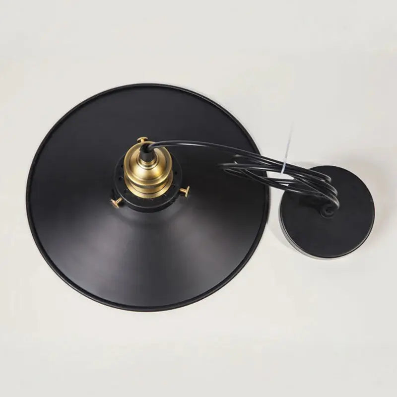 Top-down view of a black metal pendant light shade with a prominent brass lamp holder and black cable.