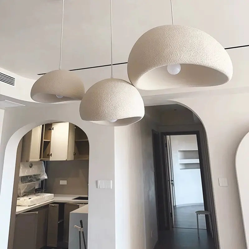 Scandinavian-style dome hanging lamps with a stone-like texture, suspended in a bright, minimalist interior with kitchen cabinets and arched features.
