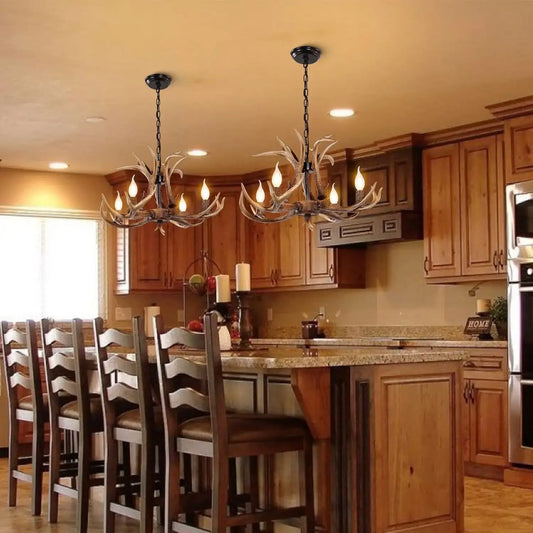 Two rustic antler chandeliers illuminating a kitchen with wooden cabinets and a large island, perfect for cabin or farmhouse decor.