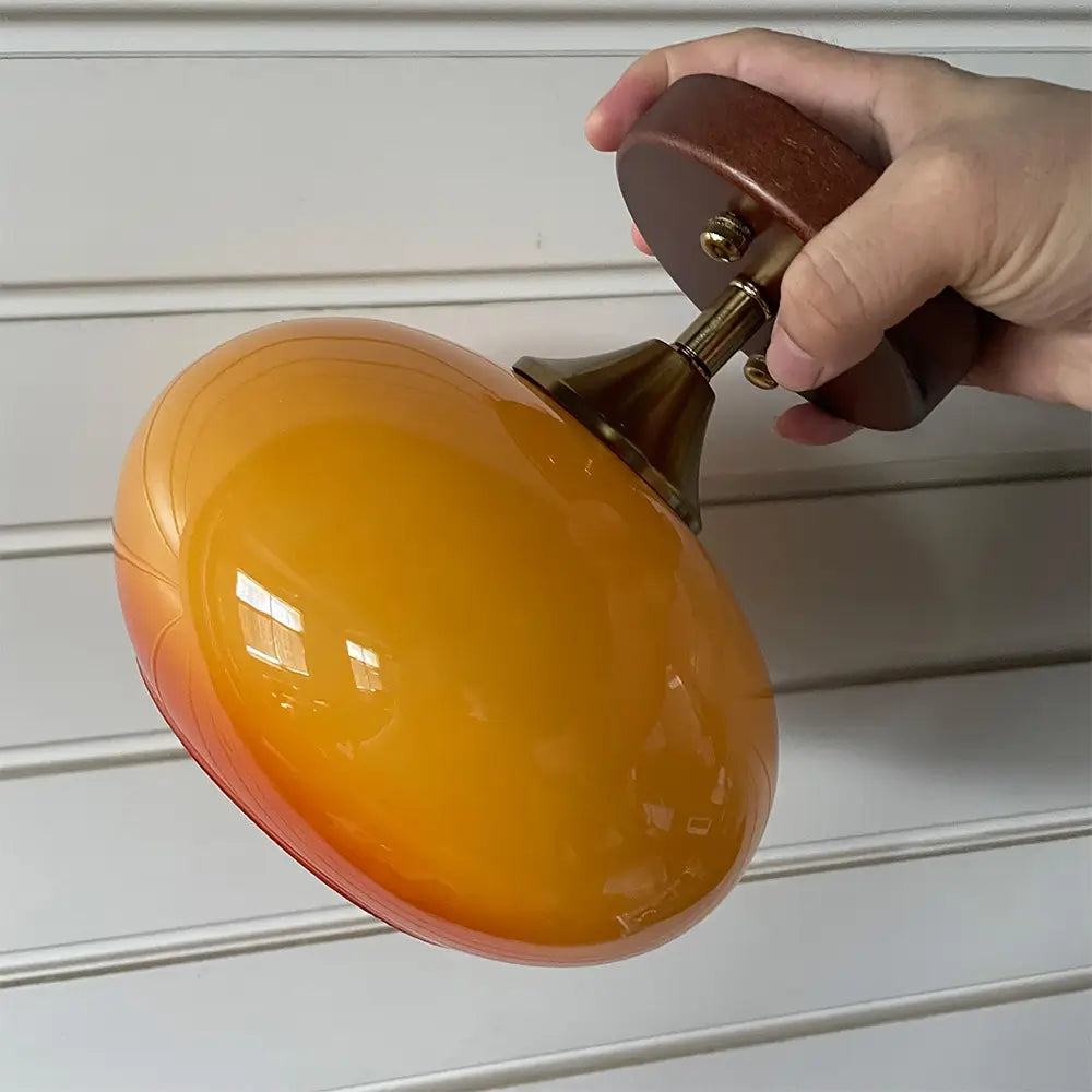 Mid-century modern orange glass ceiling lamp with a rounded shape and wood and brass details. Stylish lighting for home decor.