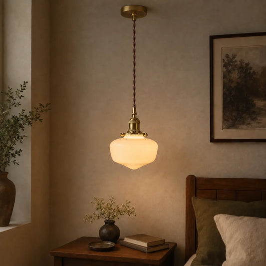 Lit opaque white glass pendant light with brass-tone hardware above a bedroom nightstand