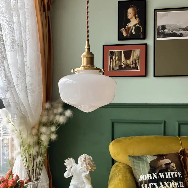 Opaque white glass pendant light with brass-tone metal hardware in a green-paneled living room