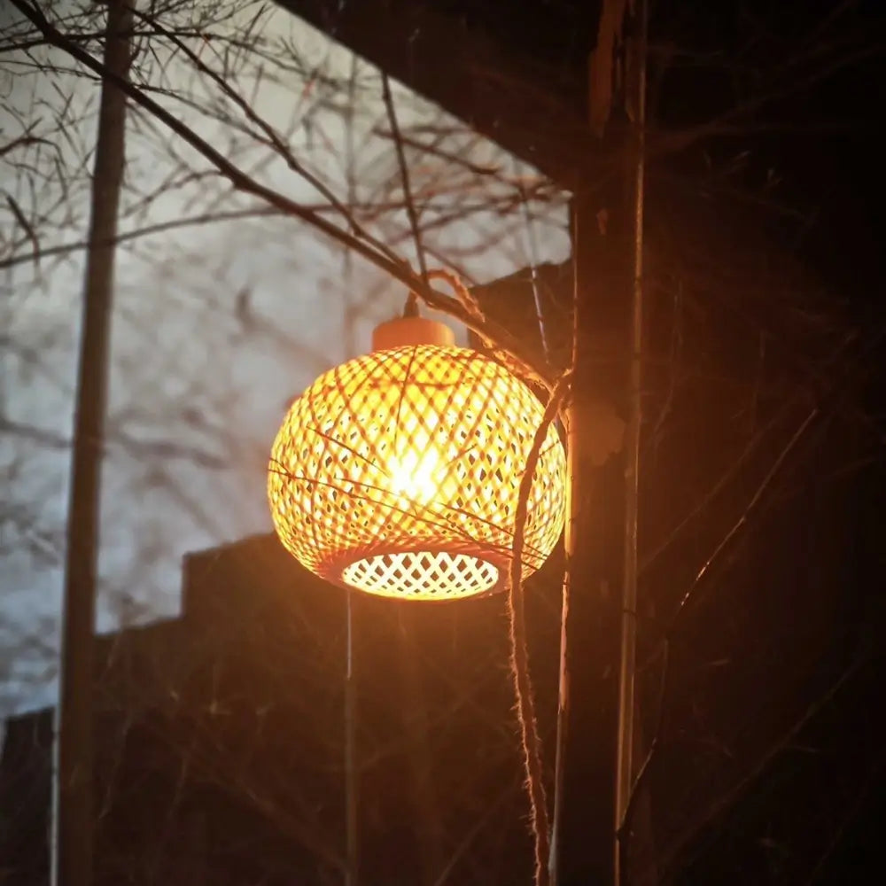 Outdoor warm lighting from bamboo hanging lamp wrapped around natural branch