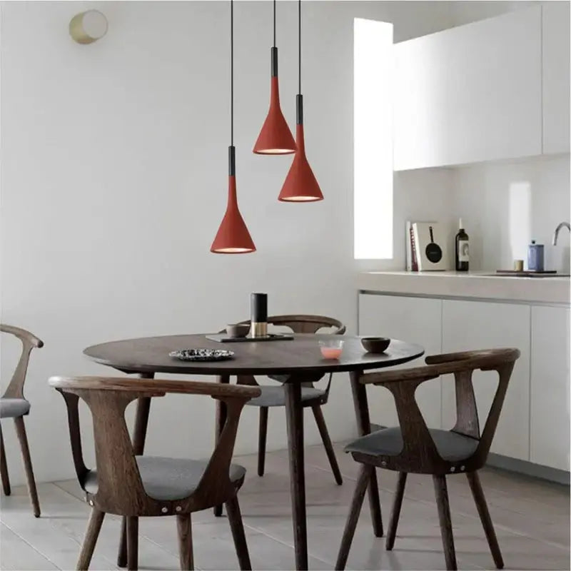 Three vibrant red modern pendant lights illuminating a circular wooden dining table with minimalist chairs, creating a focal point in a contemporary dining room.