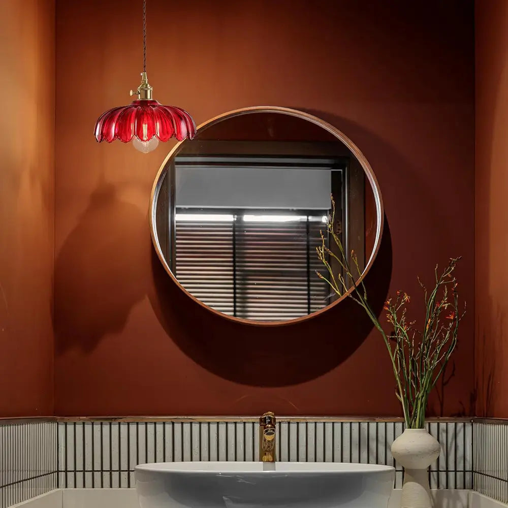 A red pendant light fixture illuminates a bathroom vanity, complementing the warm color palette and round mirror.