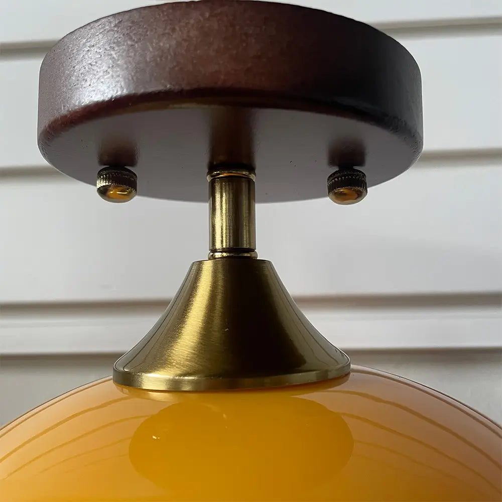 Close-up detail of a retro orange glass light fixture showing the brass stem, wooden mounting plate, and the warm-toned glass shade.
