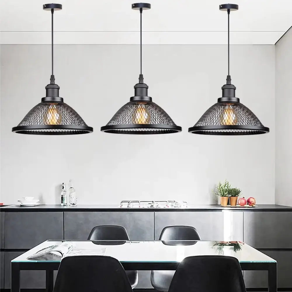Three vintage industrial black metal mesh pendant lights hanging over a modern kitchen island with black countertops and chairs, perfect for a rustic or loft design.