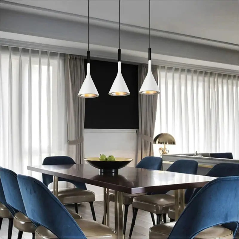 Three white modern pendant lights suspended above a long wooden dining table with blue velvet chairs, creating a chic ambiance in a dining room