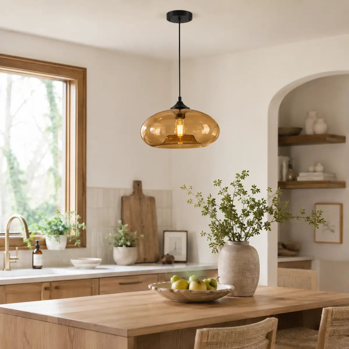 Amber oval glass pendant light installed above a wood kitchen island in a warm neutral interior.