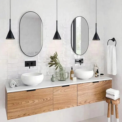 Two elegant black pendant lights above a double bathroom vanity with oval mirrors and white sinks, offering contemporary bathroom lighting for homes.