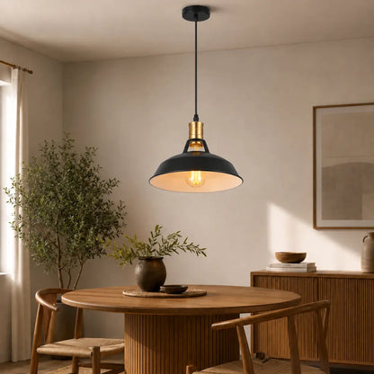 Single matte black dome pendant light above a round wood dining table in a warm modern interior.