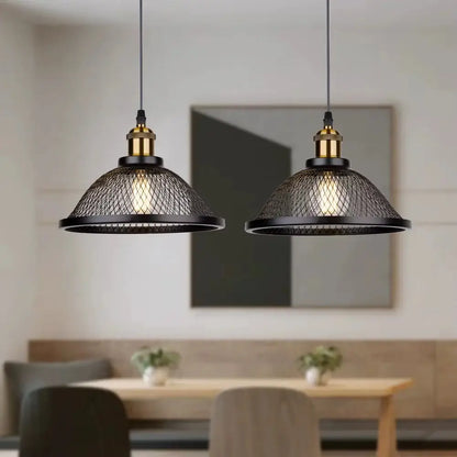 Two black industrial style hanging pendant lights with mesh shades and brass hardware, illuminating a cozy kitchen or dining area with a wooden table and bench seating.