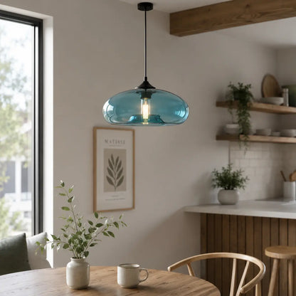 Blue oval glass pendant light hanging above a round wood table beside a modern kitchen.