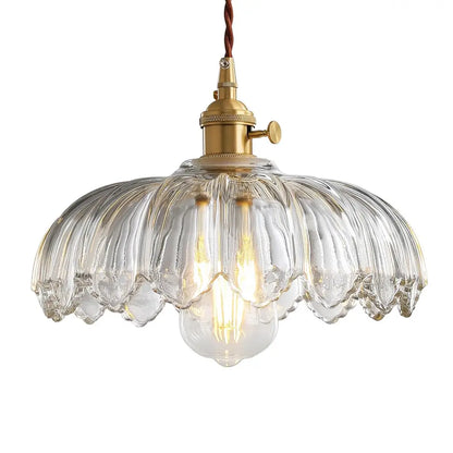 A close-up of a clear fluted glass pendant light with a scalloped shade and vintage brass fixture, showing the detailed design.