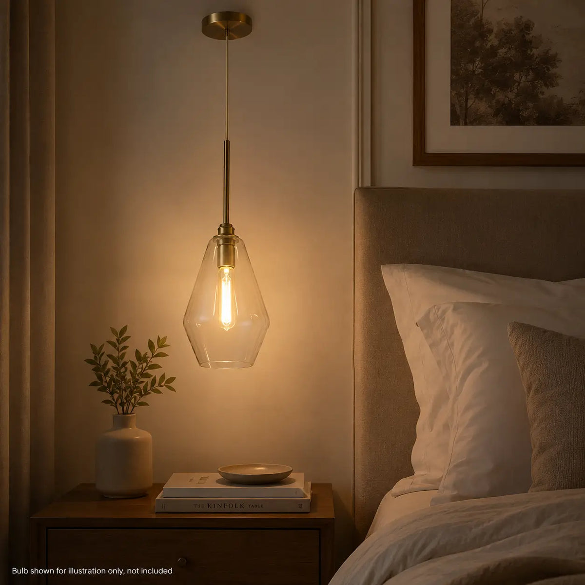 Illuminated clear glass pendant light with warm gold accents hanging beside a bed.