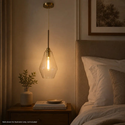 Illuminated clear glass pendant light with warm gold accents hanging beside a bed.