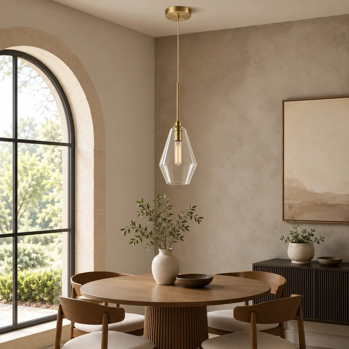 Clear glass pendant light with warm gold accents hanging above a round dining table.