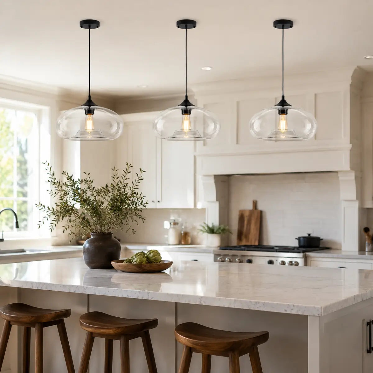 Three clear oval glass pendant lights aligned above a white kitchen island.
