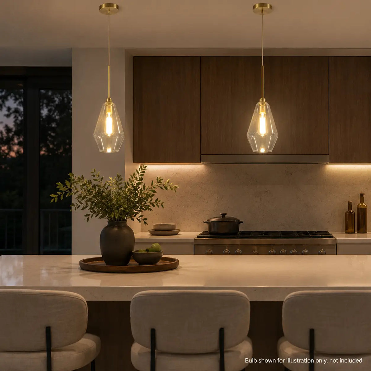 Pair of clear glass pendant lights with warm gold accents illuminated above a kitchen island.