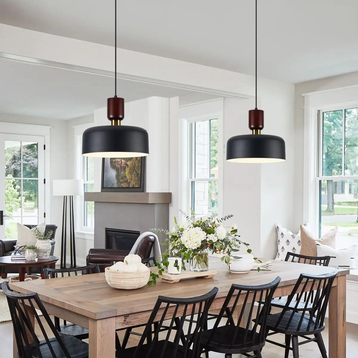 Two black pendant lights installed above a rustic dining table in a bright living room