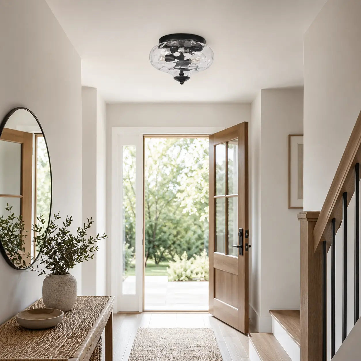 Black flush mount ceiling light installed in a bright entryway with a console table and staircase nearby.