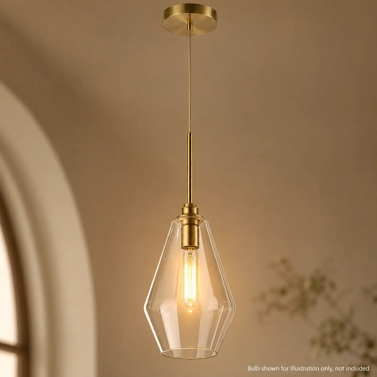 Illuminated geometric clear glass pendant light with warm gold metal accents in a neutral interior.
