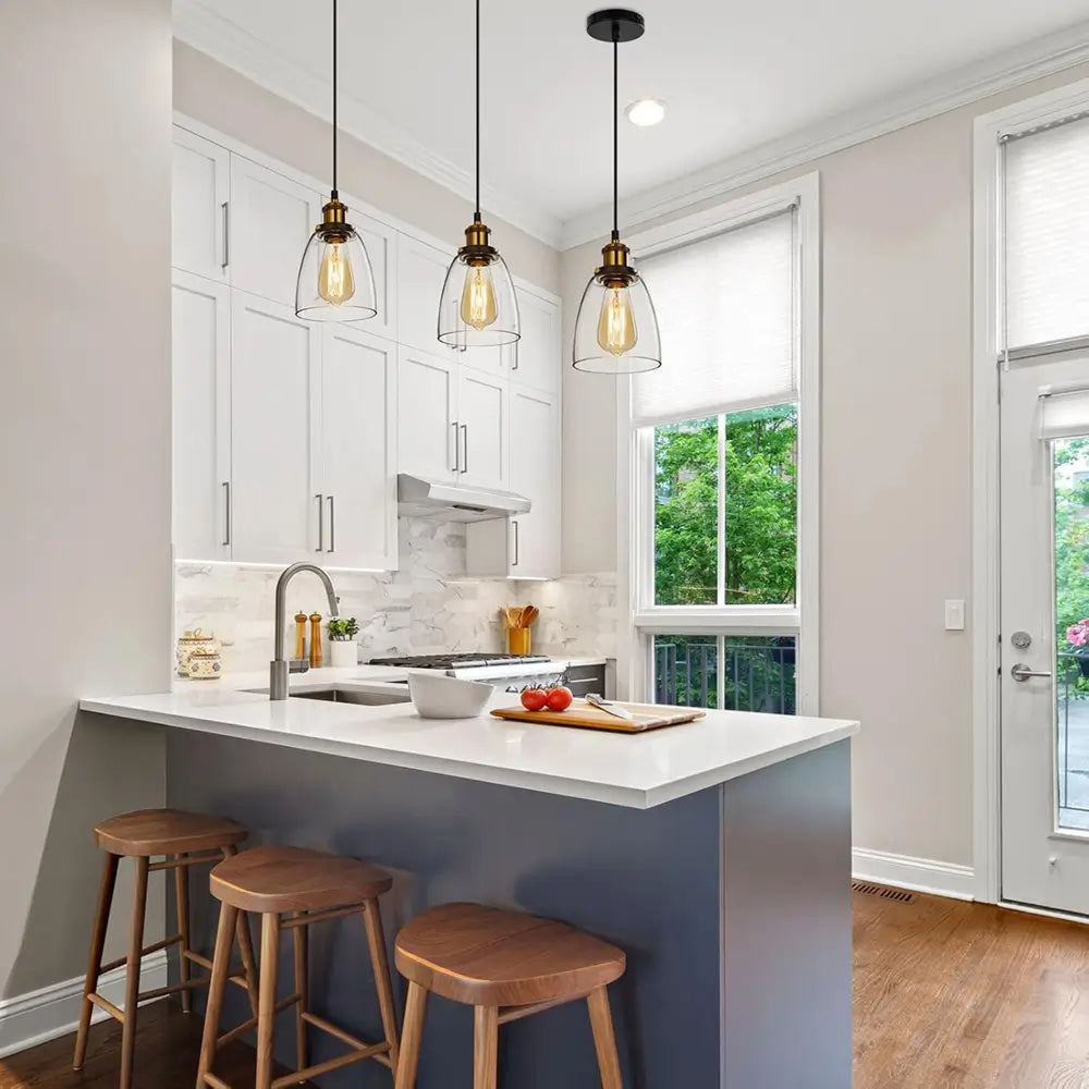 Three vintage glass pendant lights illuminating a white kitchen island with wooden bar stools.