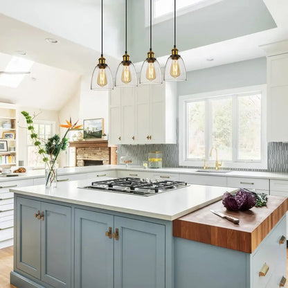 Four vintage glass pendant lights hanging over a large kitchen island in a spacious, light-filled kitchen.