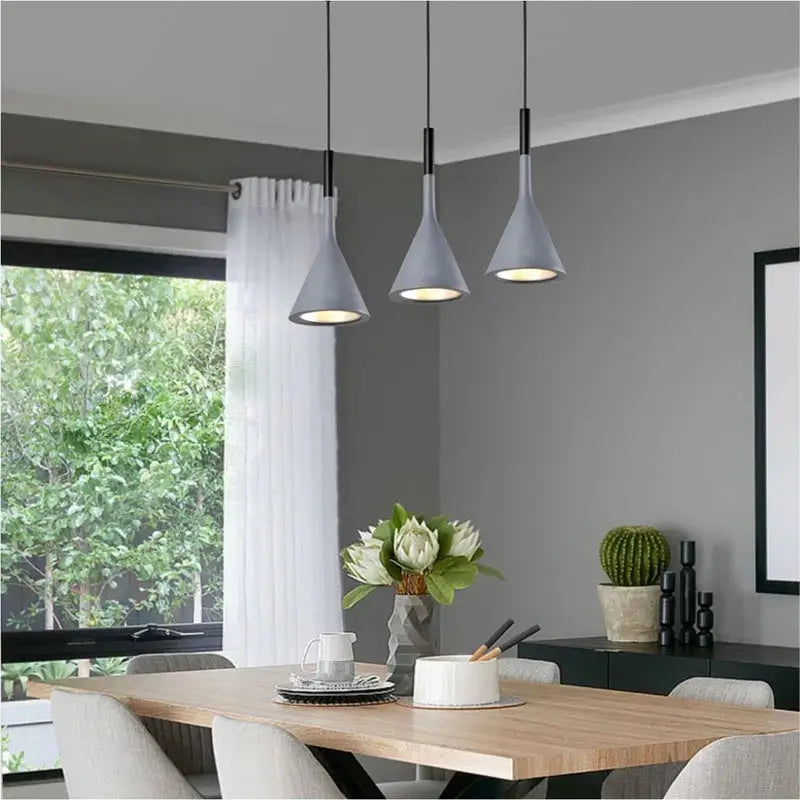 Three modern grey pendant lights illuminating a minimalist dining room with a wooden table, perfect for contemporary homes. Adjustable height ceiling lights