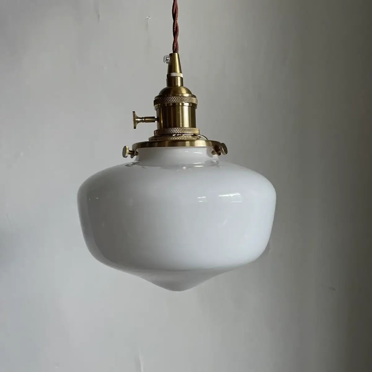 Rounded milk glass pendant light shade hanging against a plain wall