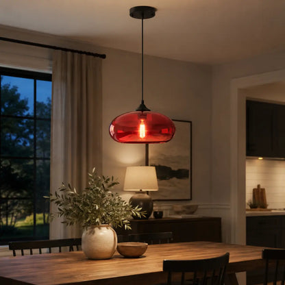 Red oval glass pendant light illuminated above a dining table in an evening interior.