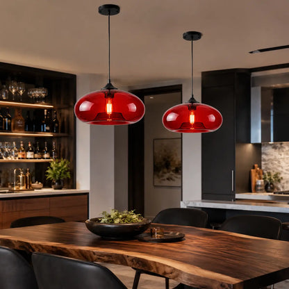 Two red oval glass pendant lights hanging above a live-edge dining table in a modern kitchen.