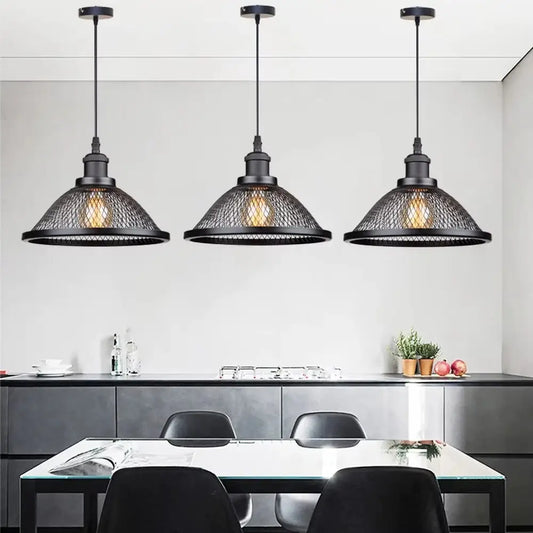 Three vintage industrial black metal mesh pendant lights hanging over a modern kitchen island with black countertops and chairs, perfect for a rustic or loft design.