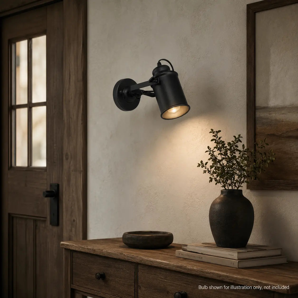 Matte black wall sconce lighting a console table near a front door